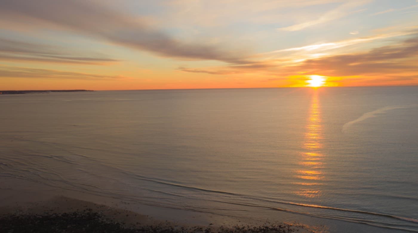 Un lever de soleil orangé sur une mer calme, vu depuis la plage