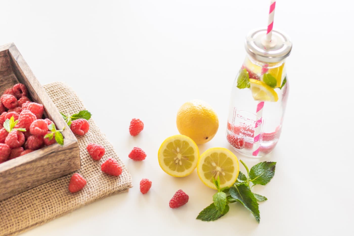 Une bouteille d'eau aromatisée au citron et à la menthe, entourée de framboises et de citrons coupés