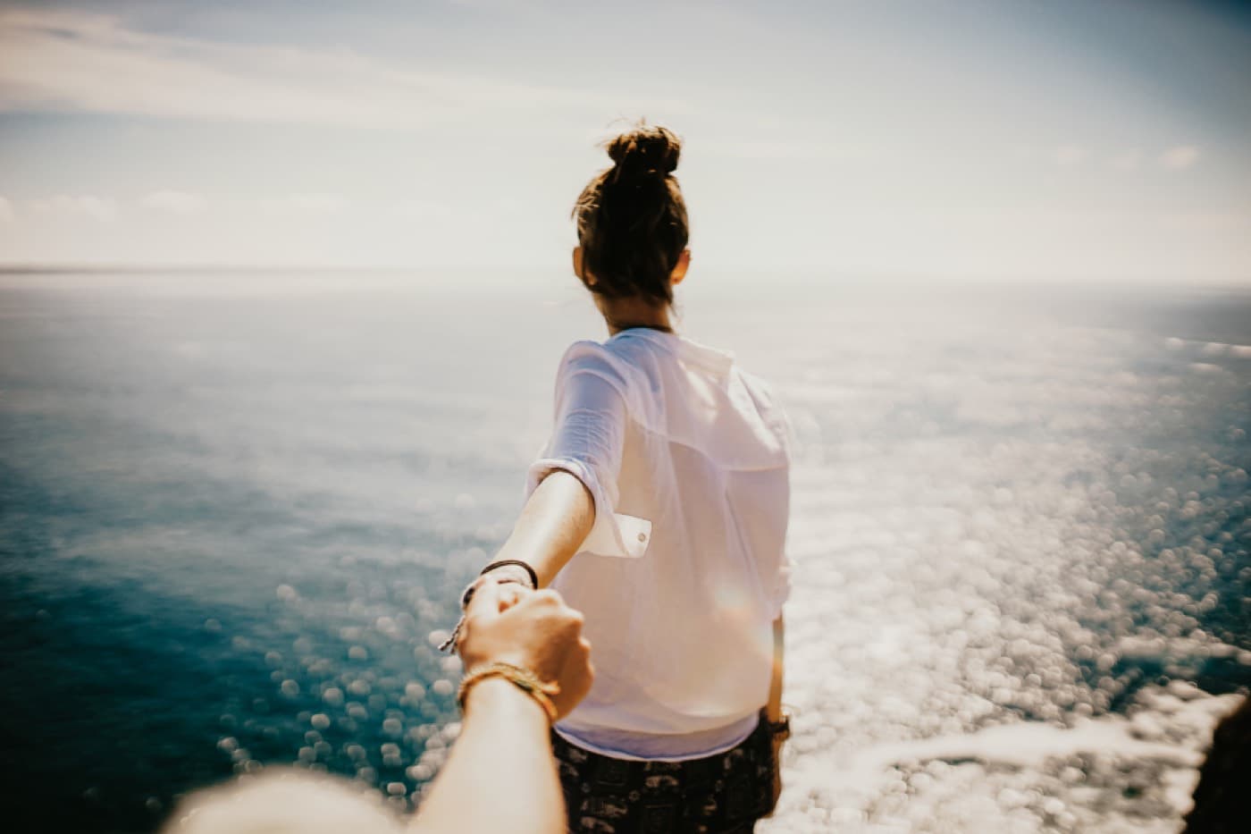 Une femme marche face à la mer, la main tendue vers la personne qui la suit
