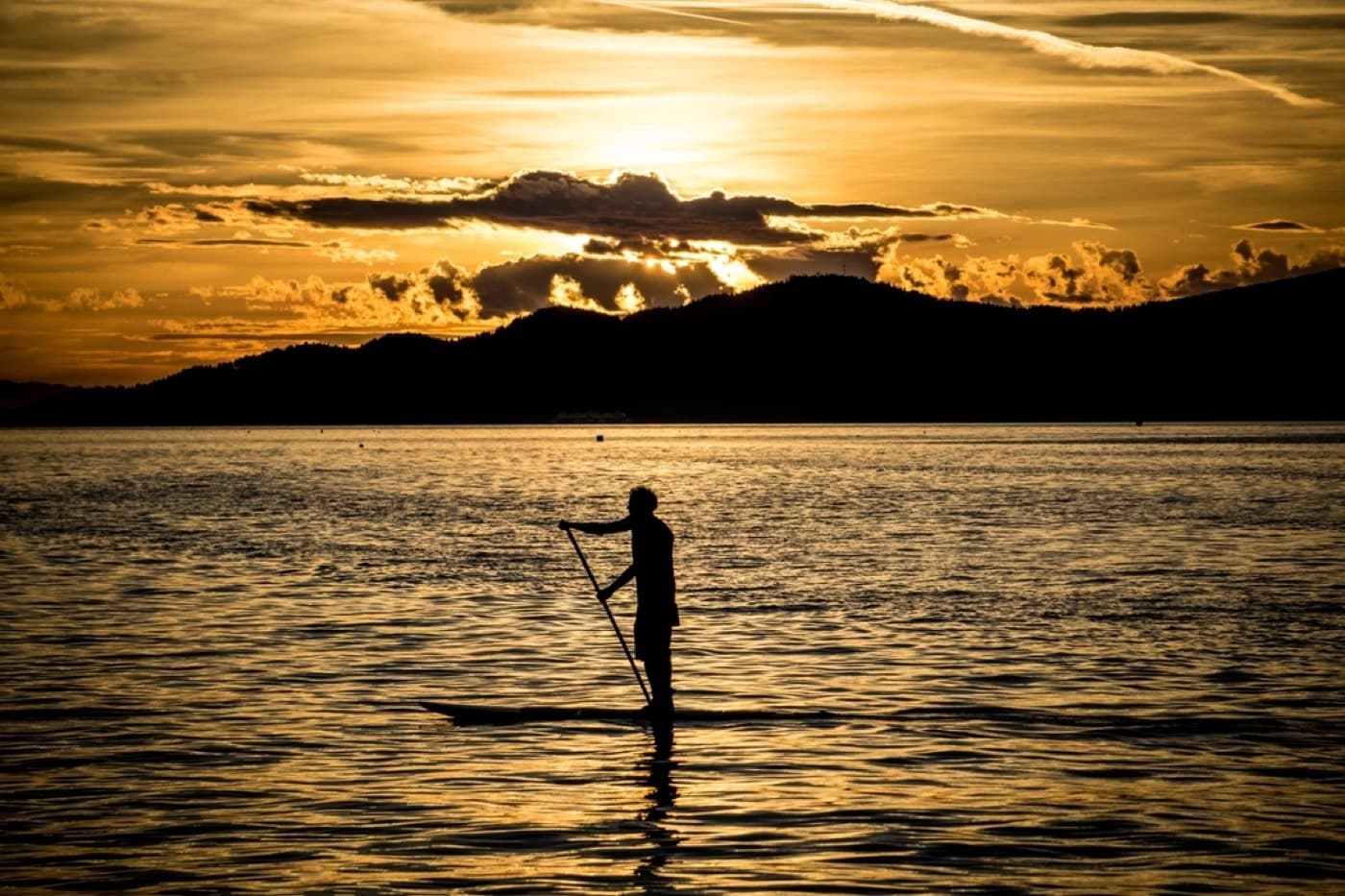 La silhouette d'une personne debout sur un paddle, au coucher du soleil