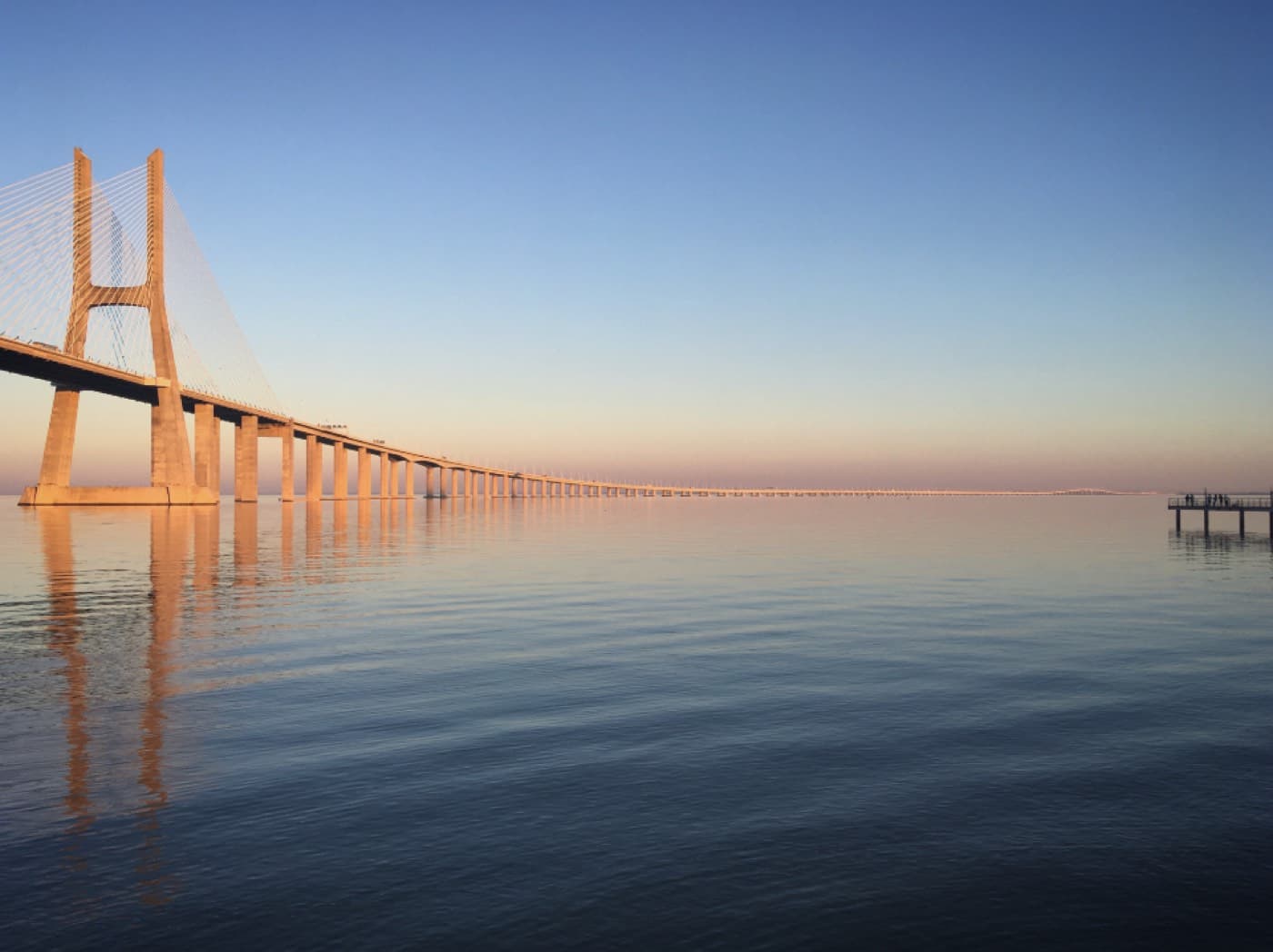 Un long pont au-dessus d'une eau calme, à la tombée du jour