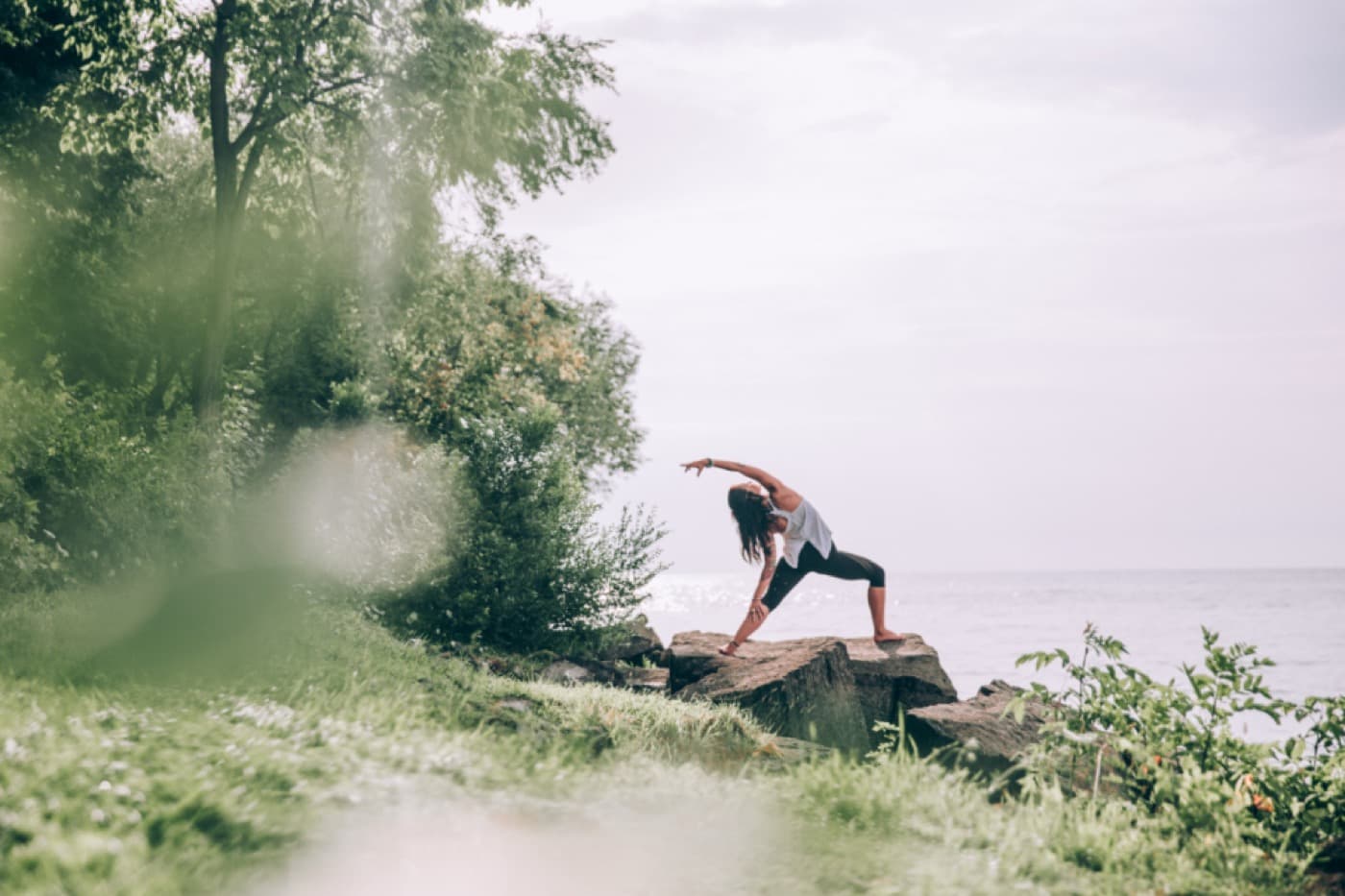 Une femme en posture de yoga sur un rocher au bord de l'eau, entourée d'arbres
