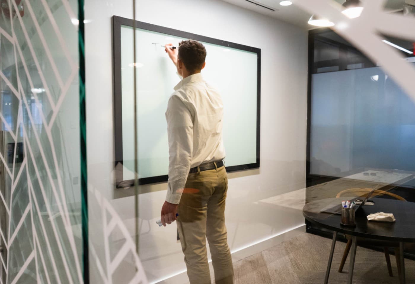 Un homme debout devant un tableau blanc dans une salle de réunion vitrée