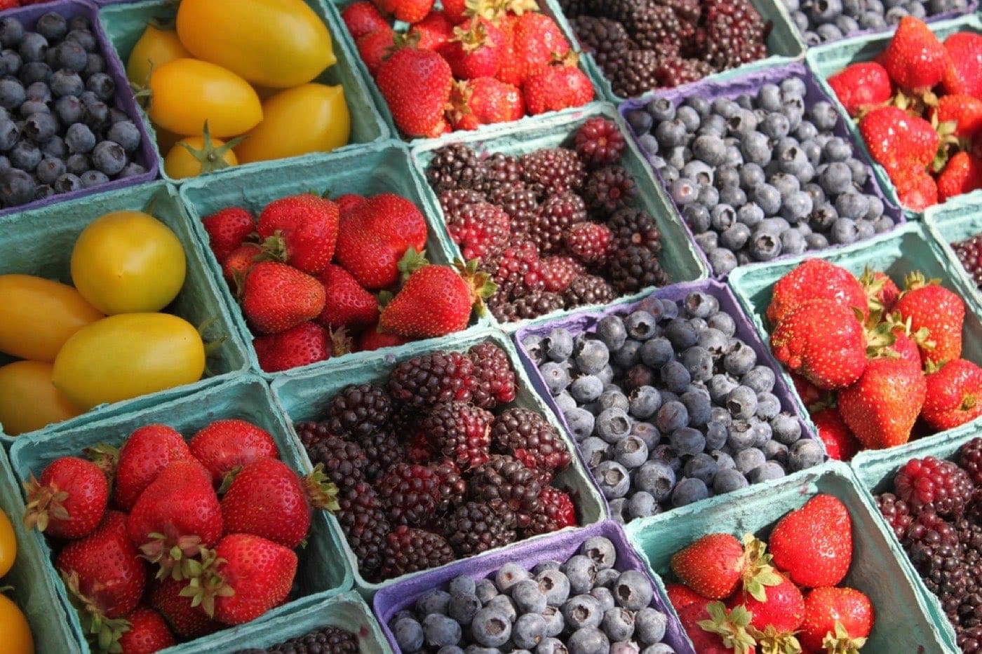 Des barquettes de fraises, de mûres, de myrtilles et de tomates jaunes sur un étal de marché