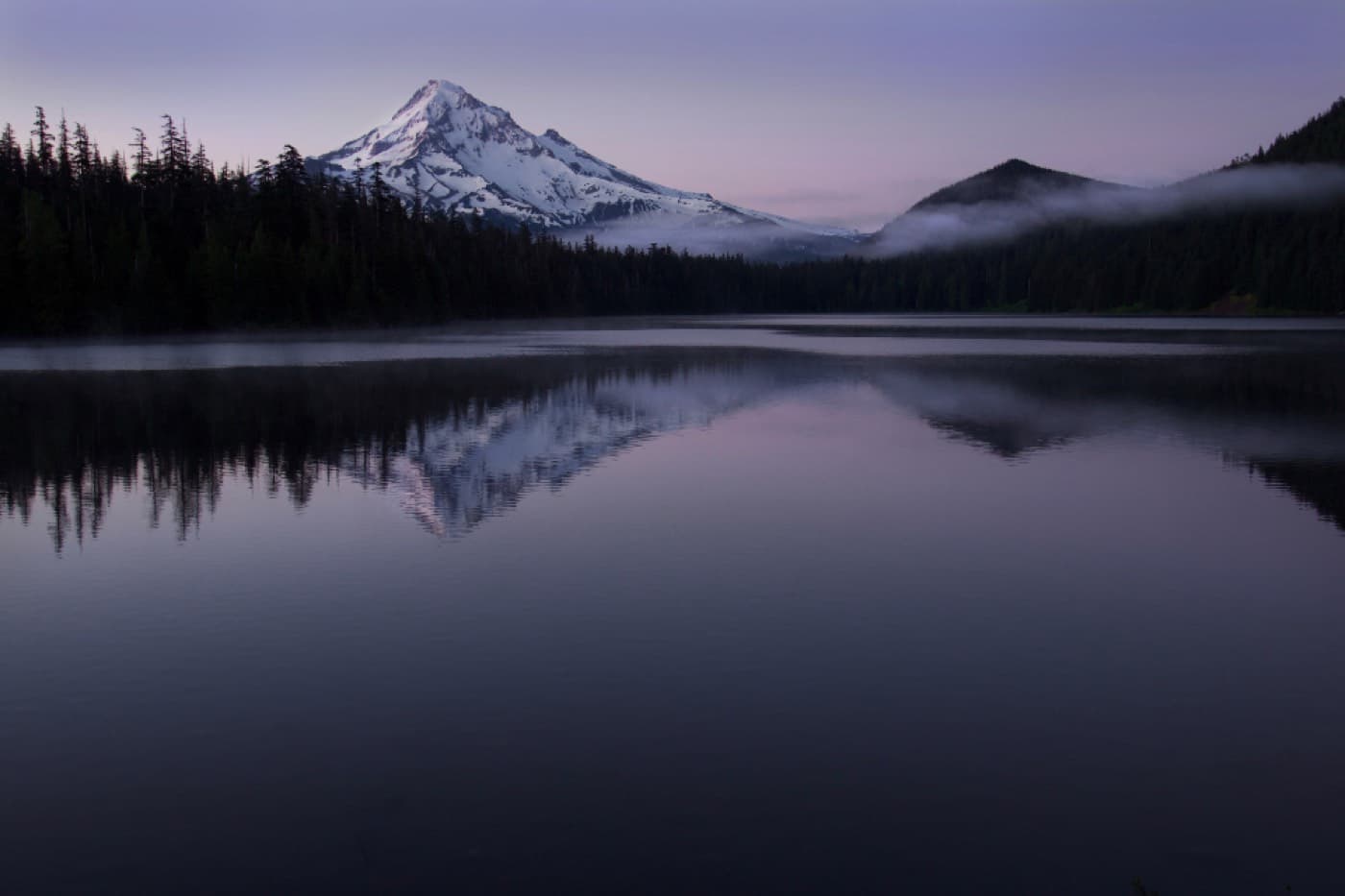 Un lac de montagne parfaitement immobile au crépuscule, reflétant un sommet enneigé