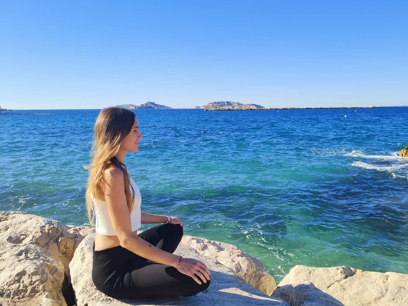 Virginia Philippe assise sur les rochers face à la mer à Marseille